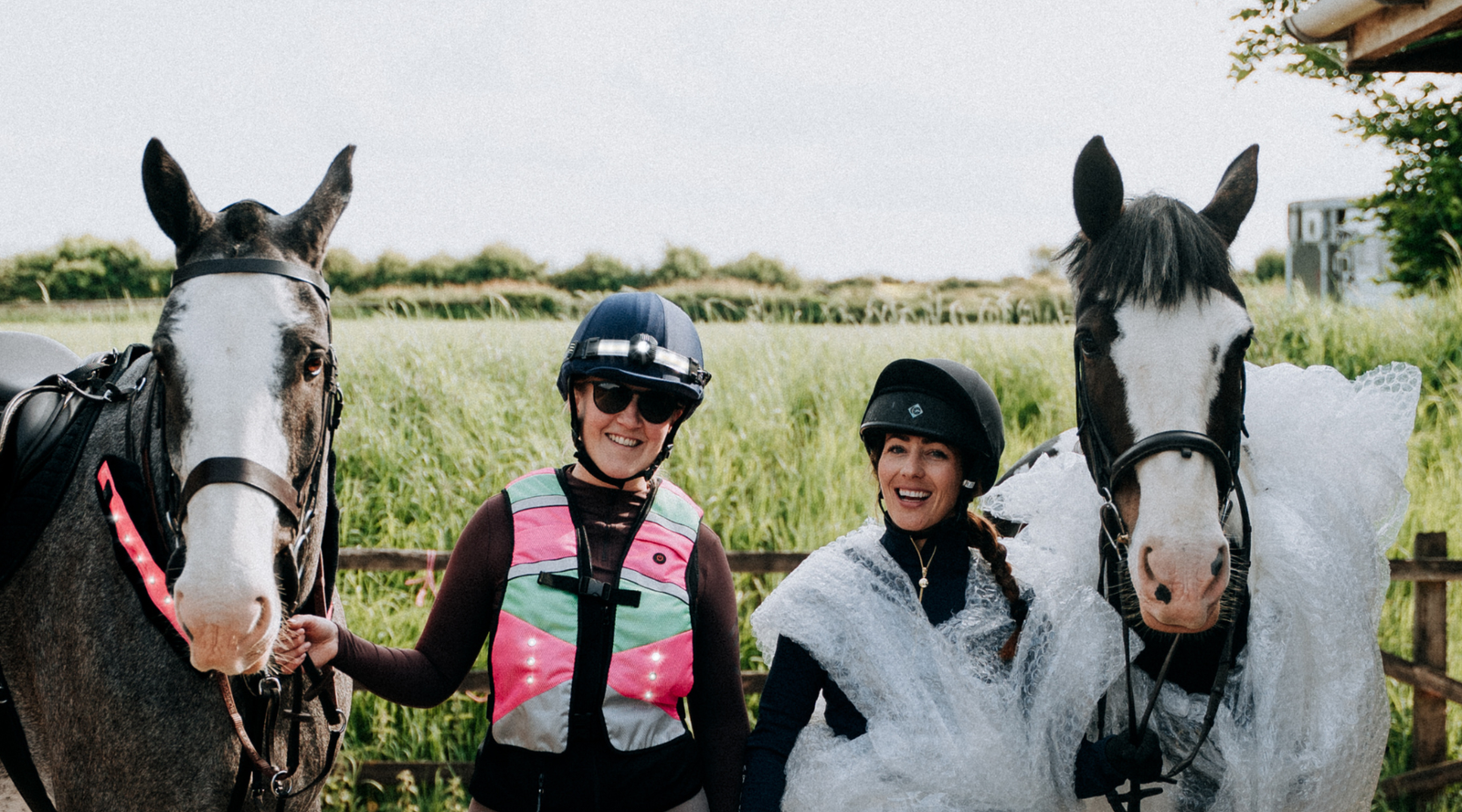 “Horse riders wearing LED visibility vests in shaded country lane” “Summer horse riding visibility in changing light conditions” “Equestrian LED visibility vest for country lane riding” “Horse rider wearing active LED visibility in woodland”