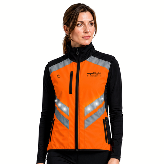 Woman wearing an orange and black equilight Sola Hi-Vis gilet with white LED lights illuminated along the front reflective panels, worn over a black long-sleeve top